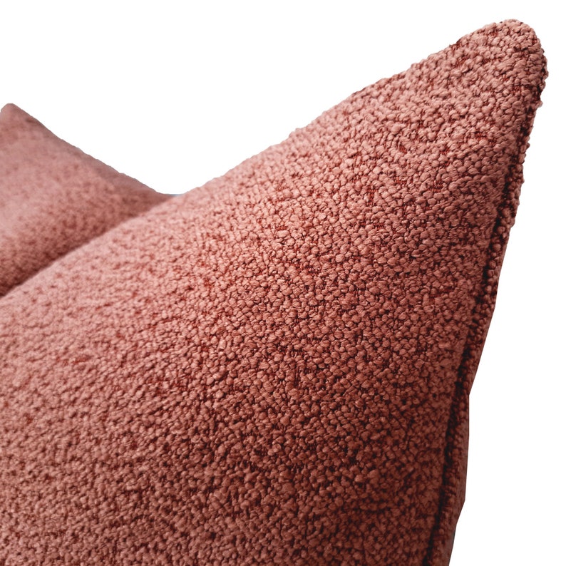 May include: Close-up of a soft, textured, terracotta-colored throw pillow. The pillow has a subtle, woven pattern and a slightly rounded shape.