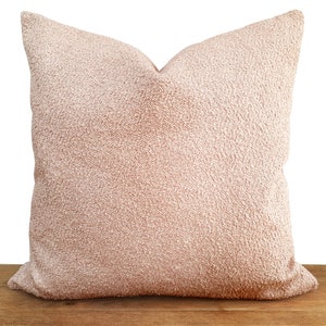 May include: A soft, plush pillow with a light pink, textured fabric. The pillow is square shaped and has a simple design.