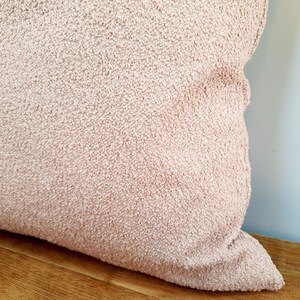 May include: A soft, plush pillow with a light pink, fuzzy texture. The pillow is made of a fluffy, comfortable material.