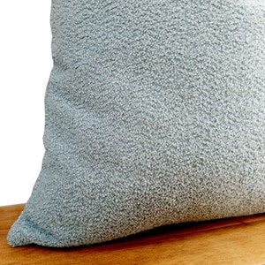 May include: A light blue throw pillow with a textured fabric. The pillow is sitting on a wooden surface.