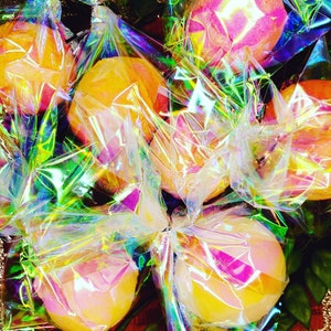 Könnte beinhalten: Eine Gruppe von Orangen, die in regenbogenfarbene Plastikfolie verpackt sind. Die Orangen sind kreisförmig angeordnet und werden von einer hellen Lichtquelle beleuchtet. Die Plastikfolie erzeugt einen farbenfrohen und abstrakten Effekt.