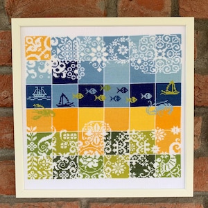 Könnte beinhalten: Gerahmtes Kreuzstich-Kunstwerk mit einem Patchwork-Design, das nautische und florale Motive aufweist. Die Farbpalette umfasst Blau-, Gelb-, Grün- und Weißtöne. Das Kunstwerk ist in einem cremefarbenen Rahmen eingefasst.