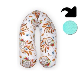 May include: A white pregnancy pillow with a U-shape design. The pillow is covered in a white fabric with a pattern of brown feathers, dreamcatchers, and flowers. The pillow is filled with a soft, supportive material.
