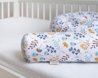 May include: A white, blue, and brown patterned baby nest with a white background and a floral design. The nest is made of soft fabric and is designed to provide a safe and comfortable sleeping space for a baby. The nest is labeled "LOOLAY".