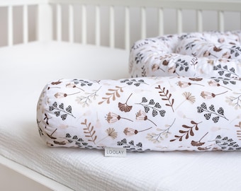 Pode incluir: Um travesseiro de amamentação branco e marrom com um design floral. O travesseiro está em um colchão de berço branco e tem a palavra "LOOLAY" impressa.