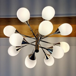 Könnte beinhalten: Eine moderne Deckenleuchte mit Chrom-Finish und mehreren weißen, kugelförmigen Lichtern. Die Leuchte hat eine zentrale Nabe mit radialen Armen, die jeweils einen Milchglas-Globus halten. Das Design ist schlank und modern, passend für verschiedene Einrichtungsstile.