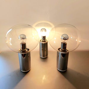 Könnte beinhalten: Drei Tischlampen aus Chrom mit klaren Glasschirmen und eingeschalteten Glühbirnen.