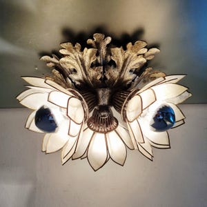 Könnte beinhalten: Verzierte Deckenleuchte mit drei blütenförmigen Schirmen. Die Schirme sind weiß mit goldfarbenem Rand, und die Glühbirnen sind tiefblau. Die Leuchte hat ein dekoratives, goldfarbenes Blattdesign.