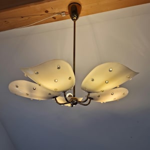 Könnte beinhalten: Ein Kronleuchter im Retro-Stil mit fünf cremefarbenen, blattförmigen Glasschirmen. Jeder Schirm ist mit kleinen, transparenten Dekorationselementen versehen. Die Leuchte hat einen messingfarbenen Stiel und eine zentrale Lichtquelle.