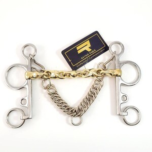 May include: A silver and gold horse bit with a chain attached. The bit has two rings on each side and a centre bar with a gold chain. The chain is attached to the centre bar with a small ring. The bit is labelled "Retro Surg Quality tools & Equestrian products".