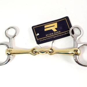 May include: A 5 inch gold and silver horse bit with a loose ring on each end. The bit has a small, round, gold-coloured logo on the centre bar.
