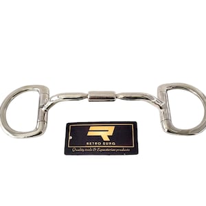 May include: A polished metal D-ring horse bit with the text "RETRO SURG" on the center bar. The bit has a curved mouthpiece and two D-shaped rings. A black tag with the brand name and "Quality tools & Equestrian products" is below.