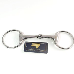 Puede incluir: Un bocado de caballo plateado con un anillo suelto en cada extremo. El bocado tiene una pequeña boquilla articulada redondeada. El bocado está sobre un fondo blanco. El texto "Retro Surg Quality tools & Equestrian products" está en una etiqueta negra y dorada.