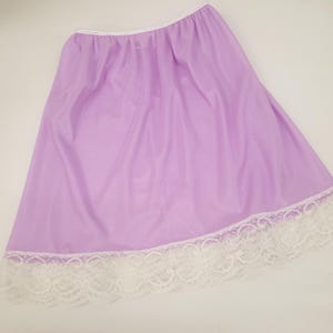 Op de afbeelding: Een lavendelkleurige halfslip met een witte kanten rand langs de zoom. De slip heeft een elastische tailleband en is gemaakt van een gladde, lichtgewicht stof. De kanten rand voegt een delicate touch toe aan het kledingstuk.