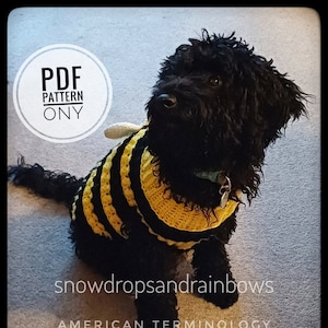 May include: A black dog wearing a yellow and black crocheted bee costume. The costume has black and yellow stripes and a white wing. The dog is sitting on a beige carpet. The text "PDF PATTERN ONLY" is in a white circle on the left side of the image. The text "snowdropsandraibows AMERICAN TERMINOLOGY" is at the bottom of the image.