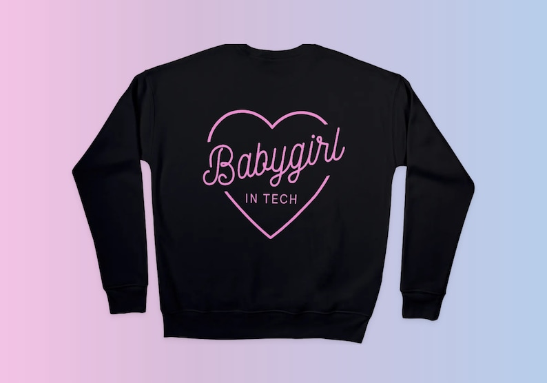 Op de afbeelding: Zwarte sweatshirt met een roze hartafbeelding en de tekst "Babygirl IN TECH" in een sierlijk lettertype. Het ontwerp is gecentreerd op de achterkant van de sweatshirt. De achtergrond heeft een roze en blauwe gradi&euml;nt.