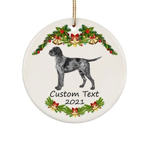 May include: A white ceramic Christmas ornament featuring a detailed illustration of a dog. The dog is black and gray, standing in profile. The ornament is decorated with festive greenery, red berries, gold bells, and the text "Custom Text 2021".