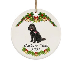 Puede incluir: Adorno navideño de cerámica blanca con un perro negro con collar rosa. El adorno tiene un diseño festivo con acebo, campanas y el texto "Custom Text 2021". Se adjunta una cuerda dorada para colgarlo.