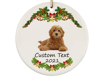 May include: A round ceramic Christmas ornament featuring a golden doodle dog with a festive garland of green pine branches, red berries, and gold bells. The ornament includes the text "Custom Text 2021".
