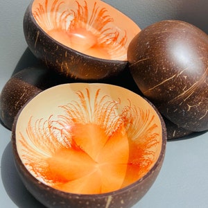May include: Several coconut bowls with a natural brown exterior and a vibrant orange and cream interior design. The bowls are grouped together, highlighting their unique textures and colours, ideal for serving food or as decorative items.