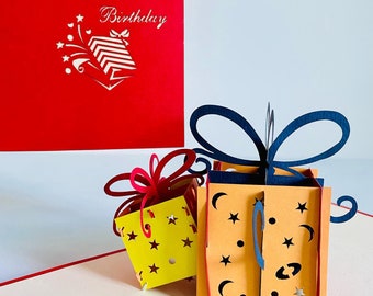 May include: A red card with the text "Happy Birthday" and a small gift box with stars. The card is open to reveal a 3D pop-up card with two gift boxes. One gift box is yellow with stars and a red bow. The other gift box is orange with stars and a blue bow.