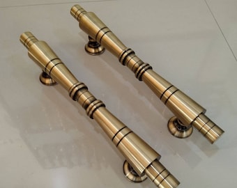 May include: Two antique gold door handles with a decorative design. The handles are made of metal and have a cylindrical shape.