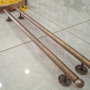 May include: Two antique brass towel bars with round finials and round mounting plates. The bars are mounted on a tiled floor.