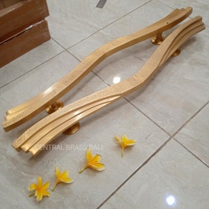 May include: A pair of gold-toned door handles with a wavy design. The handles are made of brass and have a textured finish. The handles are laid out on a tiled floor with yellow flowers.