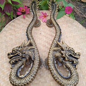 May include: A pair of gold-toned dragon door handles with intricate details. The handles are shaped like dragons with their heads facing forward and their tails curled around the handle.
