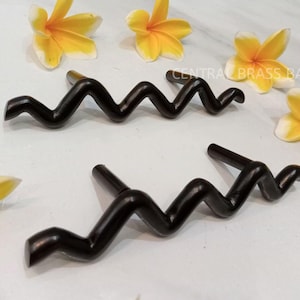 May include: Two black wavy cabinet knobs with a zig-zag design. The knobs are made of metal and have a smooth, polished finish.