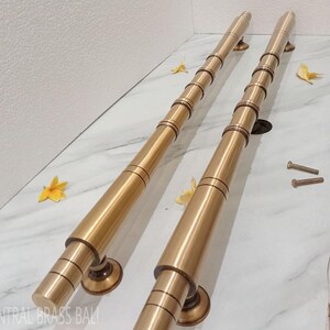 May include: Two brass door handles with a cylindrical design. Each handle has a series of circular bands and a round base. The handles are a warm gold color and are placed on a white marble surface.