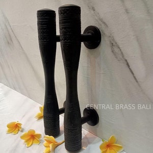 Puede incluir: Un par de tiradores de puerta negros tallados intrincadamente con un patrón geométrico. Los tiradores están montados en una pared blanca con el texto "CENTRAL BRASS BALI" visible.