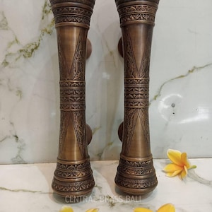 Op de afbeelding: Twee bronzen deurklinken met ingewikkelde patronen en een cilindrisch ontwerp. De handgrepen hebben een decoratieve boven- en onderkant, met een centraal gedeelte met een gedetailleerd geometrisch ontwerp. De tekst "CENTRAL BRASS BALI" is zichtbaar.