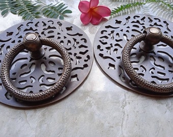 May include: Two round, ornate, brass door handles with intricate cut-out designs. Each handle features a ring pull with a textured surface.