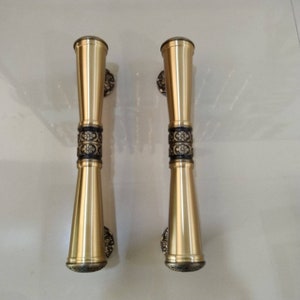 Könnte beinhalten: Zwei goldene Türklinken mit aufwendigen schwarzen und goldenen Blumendesigns. Die Griffe sind aus Metall und haben eine polierte Oberfläche.