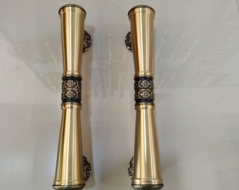 May include: A pair of gold door handles with intricate black and gold floral designs. The handles are made of metal and have a polished finish.