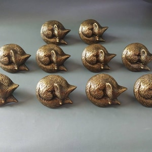May include: Ten gold-toned metal drawer pulls shaped like sleeping foxes. Each pull has a detailed design with fur and facial features.
