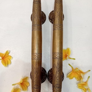 May include: A pair of ornate brass door handles with intricate geometric designs. The handles are long and slender, with a pointed tip at the top and a rounded base. The designs are etched into the metal, creating a raised effect.