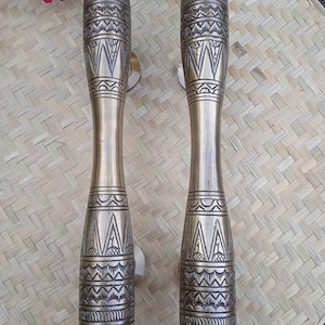 May include: Two ornate brass door handles with intricate geometric patterns. The handles are a light gold color and have a cylindrical shape.