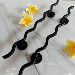 May include: Two black wavy door handles with round bases. The handles are on a white marble surface with yellow flowers.