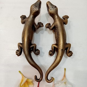May include: A pair of antique brass door handles shaped like geckos. The handles are facing each other and have a detailed design.
