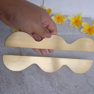 May include: Two gold-toned metal cabinet pulls with a wavy design. The pulls are brushed and have a smooth finish.