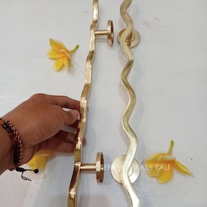 May include: Two gold-toned door handles with a wavy design. The handles are made of brass and have a polished finish. The handles are shown against a white background.