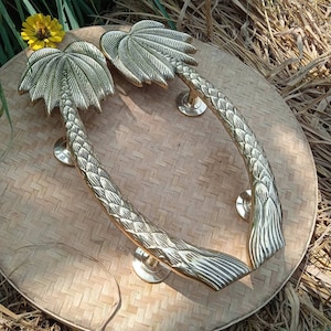 May include: Two gold palm tree door handles with intricate details. The handles are on a woven background.