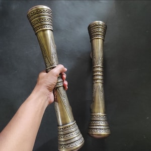 Könnte beinhalten: Zwei verzierte Türgriffe aus Messing mit komplizierten Designs. Die Griffe sind lang und zylindrisch mit einem ausgestellten Sockel. Die Griffe sind in einem satten Goldton gehalten.