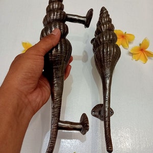 May include: A pair of ornate, bronze-colored door handles shaped like seashells. The handles have a textured, spiraled design and are attached to a metal plate.