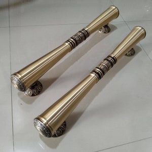 May include: Two antique brass door handles. Each handle has a cylindrical design with decorative floral patterns and black accents. The handles are mounted on circular bases with ornate detailing, suggesting a vintage or classic style.