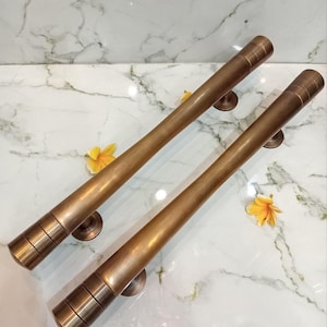 May include: Two bronze door handles with a cylindrical design. Each handle features horizontal grooves near the end and is mounted on a circular base. They are set against a white marble surface.