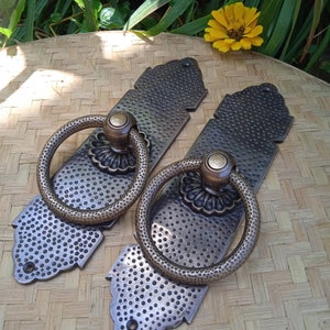 May include: Two antique brass cabinet door pulls with ornate designs and ring handles. The pulls have a hammered finish and a distressed look.