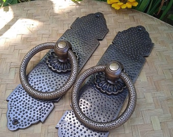 May include: Two antique brass cabinet door pulls with ornate designs and ring handles. The pulls have a hammered finish and a distressed look.